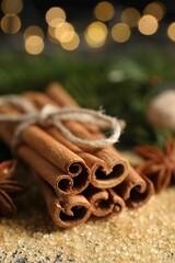 Different spices. Cinnamon sticks and cane sugar on table against blurred lights, closeup