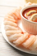 Tasty boiled shrimps with cocktail sauce and lemon on white wooden table, closeup