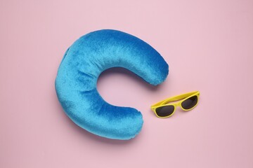 Light blue travel pillow and sunglasses on pink background, flat lay