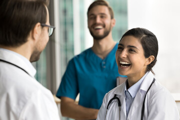 Cheerful pretty Indian doctor woman talking to male colleague in hospital office, laughing, enjoying conversation, discussing medical professional success, successful career in medicine