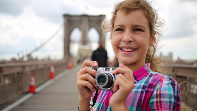 Girl photographs on Brooklyn Bridge among going people in New York