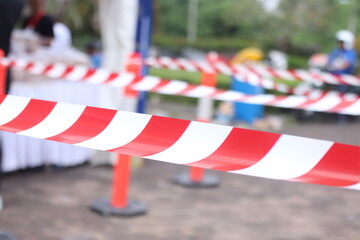 Selective focus on barricade or tape barrier in red and white with unfocused background of queuing...