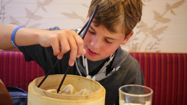 Boy tries to eat with chopsticks Chinese dumplings in cafe