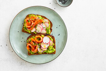 Avocado toasts with salmon, radish, and herbs on a plate. Healthy breakfast. Copy space.