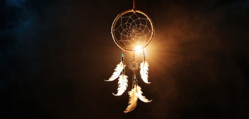  a close up of a light that has a dream catcher hanging from it's side with feathers hanging from it's sides and a dark sky with clouds in the background. - obrazy, fototapety, plakaty