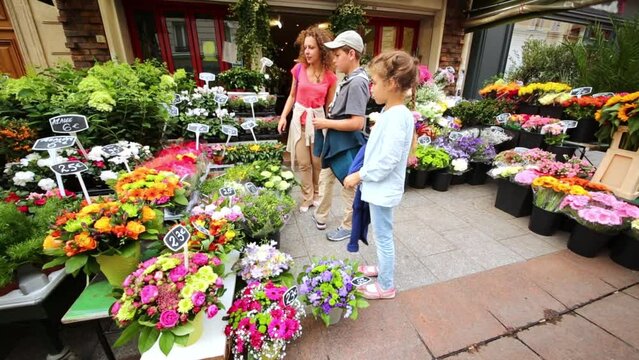 Mother and children look at flowers in flower shop on street.