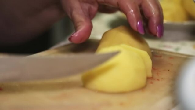 Hands of an elderly woman cutting potatoes on a cutting board.