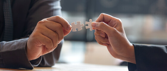 Close up Business team work holding two jigsaw connecting couple puzzle piece for matching to goals target. People success and start up new project, city background.  Business Concept