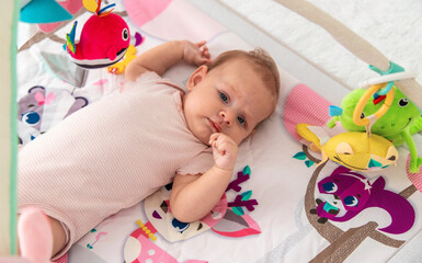 a baby plays with hanging toys on a play mat. a child, a baby plays at home