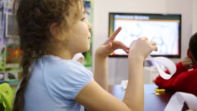 Girl with a strip of paper in hands sits and listening to teacher