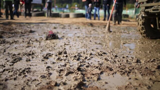 Toy SUV moves on dirt near big wheel of car outdoor