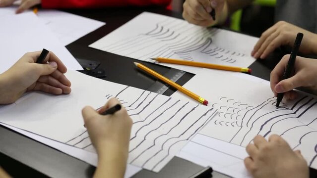 Children draws lines on painted hand by black felt-tip pen on table