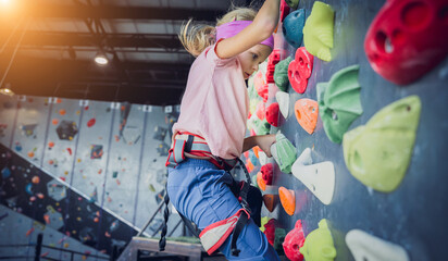A strong baby climber climbs an artificial wall with colorful grips and ropes. - obrazy, fototapety, plakaty