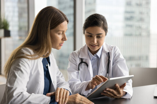 Two Serious Multiethnic Doctor Colleagues Working With Tablet Together, Reviewing Electronic Medical Records, Talking, Looking At Screen, Using Medical Application, Modern Technology For Job