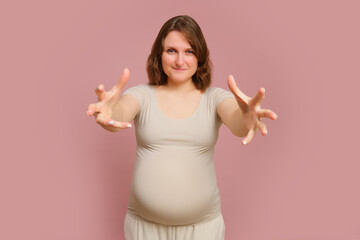 A pregnant woman stretching her arms on a studio pink background. Pregnancy in a hugging woman with a belly