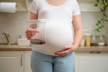 Pregnant woman holding a can of beans in her hands, home kitchen background. Pregnancy and proper...