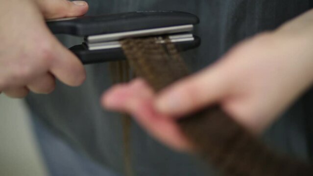 Hands of visagiste processes model hair lock with goffering-tongs
