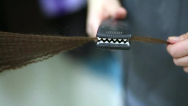 Hands of visagiste work with goffering-tongs during goffering hair