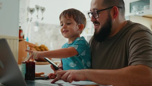Smiling father and curious little boy having breakfast in kitchen using laptop