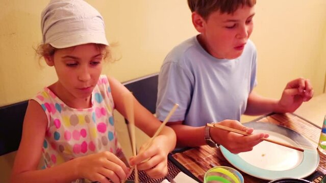 Boy and girl eat using of Chinese chopsticks at home