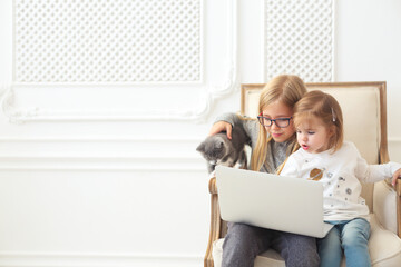 Adorable litle sisters using their computer laptop together with their kitten