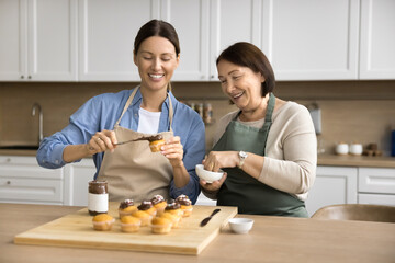 Happy old mature mother and adult child woman cooking delicious homemade dessert for family...