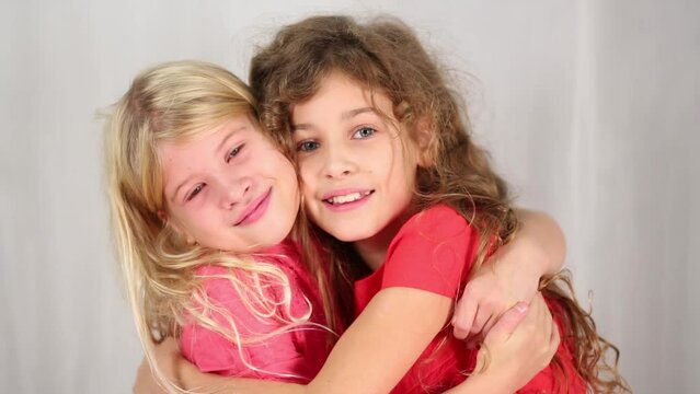 Two pretty girl in red embrace and smile in white studio
