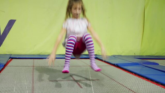 Pretty girl in dress jumps on indoor green trampoline