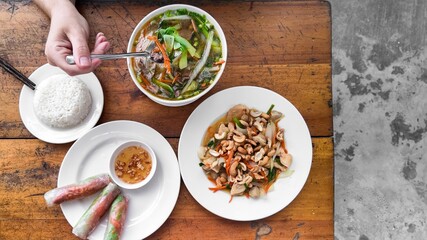 Top view of a traditional Vietnamese meal with various dishes, including pho, spring rolls, and stir-fried vegetables with cashews on a wooden table