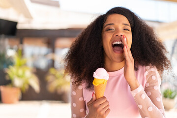 Young African American woman with a cornet ice cream at outdoors shouting with mouth wide open