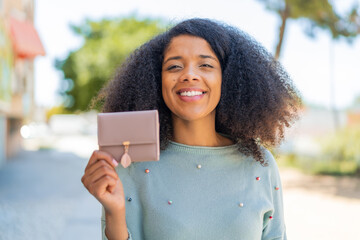Young African American woman holding a wallet at outdoors with happy expression - obrazy, fototapety, plakaty