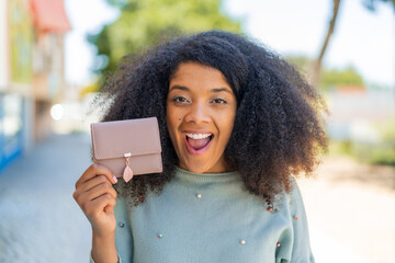 Young African American woman holding a wallet at outdoors with surprise and shocked facial...