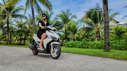 Woman enjoying a scooter ride along a palm-lined street in a tropical location, depicting summer vacation or leisure travel