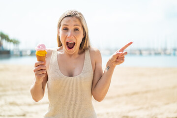 Young blonde woman with a cornet ice cream at outdoors surprised and pointing finger to the side