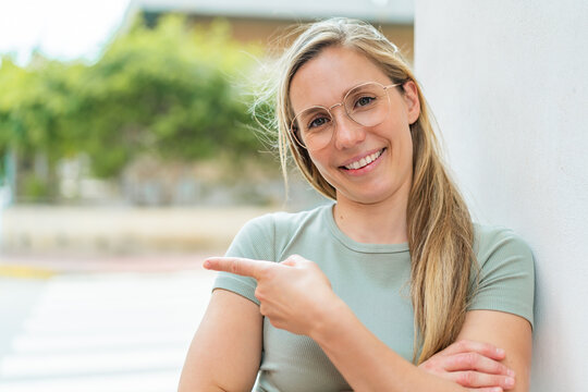 Young blonde woman at outdoors With glasses and pointing side