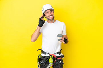 Young rock- climber man isolated on yellow background holding coffee to take away and a mobile
