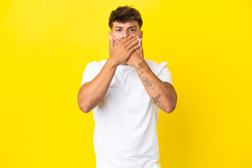 Young caucasian handsome man isolated on yellow background covering mouth with hands