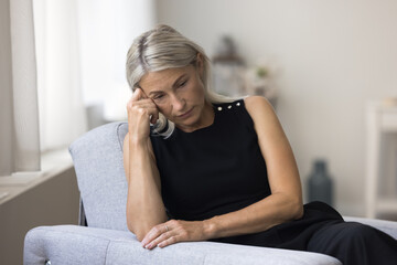 Sad melancholic mature woman sit alone at home deep in thoughts, thinking about personal life troubles, unrealized goals, marriage split feel unhappy and lonely. Middle age crisis, divorce, nostalgia