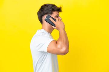 Young caucasian handsome man isolated on yellow background keeping a conversation with the mobile phone with someone