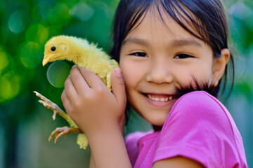 A portrait of a little smiling girl holding a yellow chick in her hands