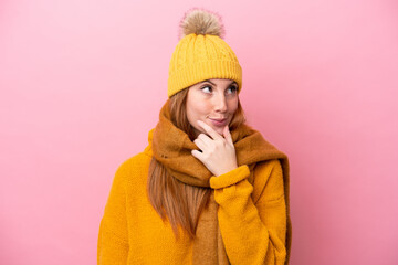 Young redhead woman wearing winter jacket isolated on pink background having doubts and with...
