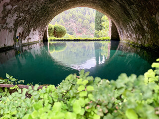 A small turquoise lake in a brick cave or vault on the holiday island of Mallorca, with a view of the mountains