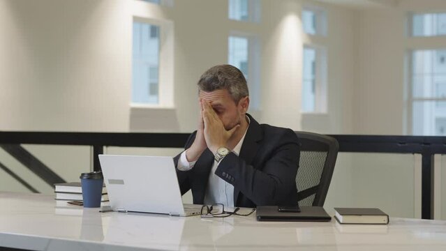 Stressed businessman working in office. Overworked tired stressed business man has headache while working in office. Stressed employee sit in office. Stressed office worker. Tired ceo manager.