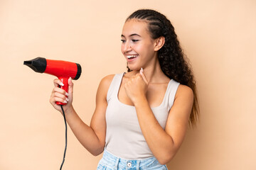 Young woman holding a hairdryer isolated on beige background celebrating a victory