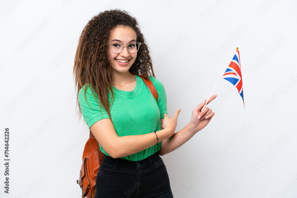 Wall mural young arab woman holding an united kingdom flag isolated on white background pointing back