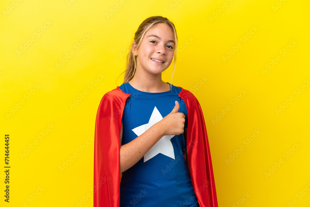 Wall mural Super Hero little girl isolated on yellow background giving a thumbs up gesture