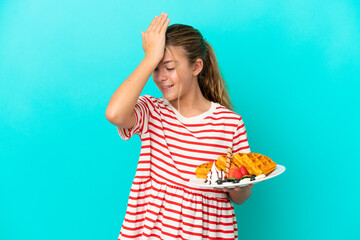 Little caucasian girl holding waffles isolated on blue background has realized something and...