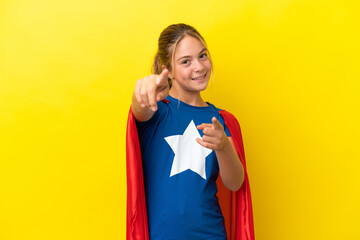 Super Hero little girl isolated on yellow background points finger at you while smiling