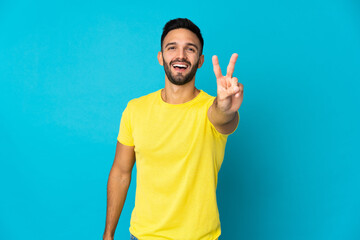 Young caucasian man isolated on blue background smiling and showing victory sign