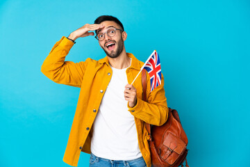 Young caucasian man holding an United Kingdom flag isolated on yellow background doing surprise gesture while looking to the side - obrazy, fototapety, plakaty